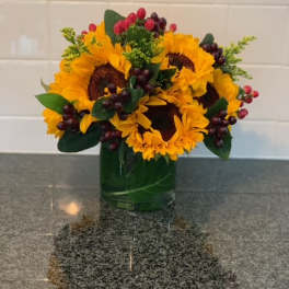 Sunflower arrangement in a green glass vase with berry accents