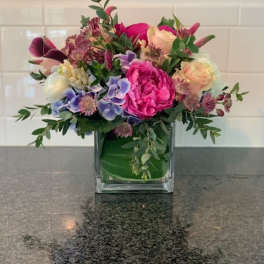 Mixed bouquet in a square glass vase with pink, peach, purple, and white blooms