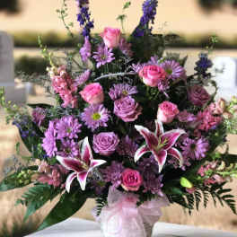 Pink and purple mixed flower arrangement in a white basket with ribbon