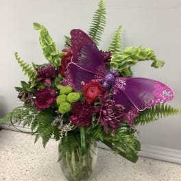 Purple butterfly decoration in a mixed flower bouquet in a glass vase