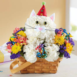 White flower cat arrangement in a basket with a party hat and colorful blooms