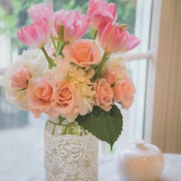 Pink tulips and peach roses arranged in a glass vase with lace wrap
