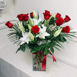 Red roses and white lilies in a clear glass vase with a red ribbon