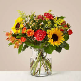 Mixed bouquet of sunflowers, roses, and carnations in a glass vase