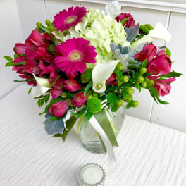 Mixed bouquet of hot pink gerbera daisies, white hydrangea, and mini calla lilies in a clear glass vase.