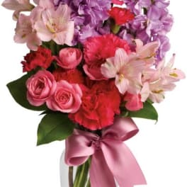 Pink and purple mixed bouquet in a clear glass vase with a ribbon