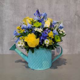 Mixed bouquet in a turquoise watering can vase with yellow and blue flowers