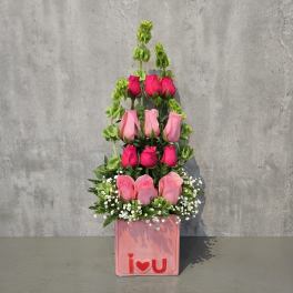 Tiered pink rose arrangement in a pink box with an "I love U" front decoration