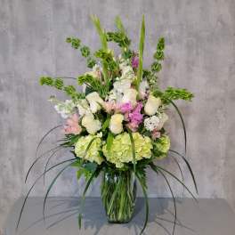 Tall floral arrangement with white roses, hydrangeas, and pink blooms in a glass vase