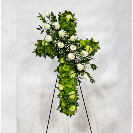 Cross-shaped floral tribute with white roses and green flowers on a stand