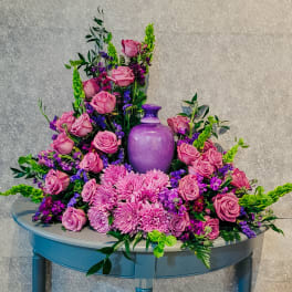 Pink roses and purple flowers arranged around a purple vase on a table