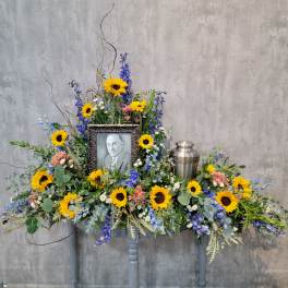 Large memorial floral arrangement with sunflowers and a framed portrait
