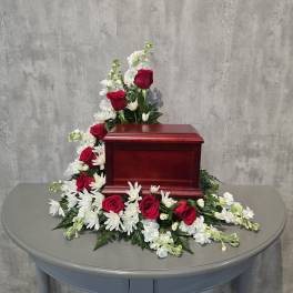 Red roses and white flowers arranged around a wooden urn