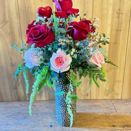 Bouquet of red and pink roses in a tall patterned vase with a heart accent