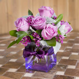 Pink roses arranged in a purple glass vase with a ribbon