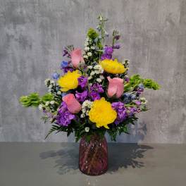 Colorful bouquet of yellow, pink, and purple flowers in a purple vase