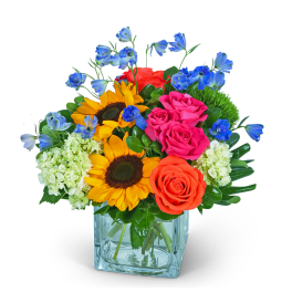 Mixed bouquet with sunflowers, roses, hydrangeas, and blue flowers in a glass vase