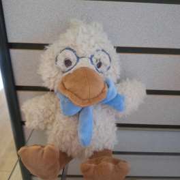 Plush duck toy with fuzzy cream fur, blue scarf, and fabric glasses on a display shelf