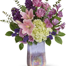 Pink lilies, roses, and purple flowers in a tall iridescent vase