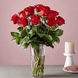 Red roses arranged in a clear glass vase beside a white candle