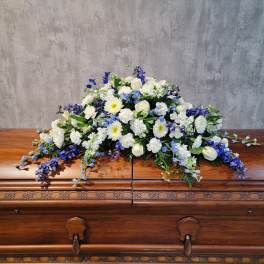 White and blue floral casket spray on a wooden casket