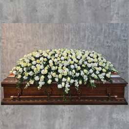 White and pale yellow floral casket spray on a wooden casket