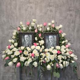 Symmetrical floral tribute with two framed portraits surrounded by white and pink roses