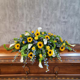 Casket spray with sunflowers, white calla lilies, yellow roses, and blue flowers
