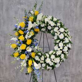 Floral wreath with yellow roses, white calla lilies, and white daisies on a stand