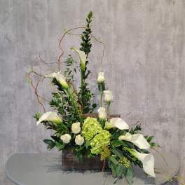 Tall floral arrangement with white calla lilies and green hydrangeas in a wooden box