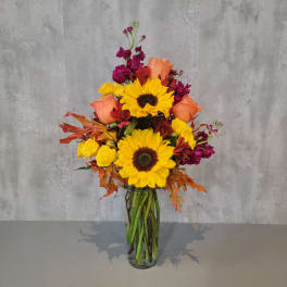 Tall bouquet of sunflowers, roses, and magenta flowers in a glass vase