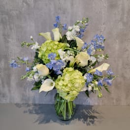 Blue and white flowers with pale green hydrangeas in a glass vase