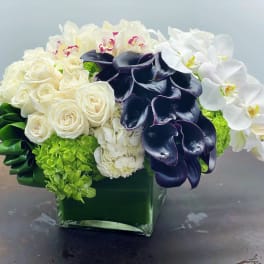 White roses, orchids, and dark calla lilies in a green glass vase