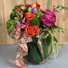 Colorful bouquet of roses and greenery in a green vase with a carrot-print ribbon