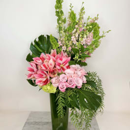 Pink roses and amaryllis in a tall green vase with tropical foliage