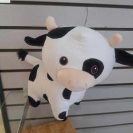Small black and white cow plush toy with pink snout on a display shelf.