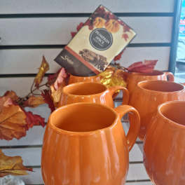 Orange pumpkin-shaped mugs displayed with autumn leaf decor