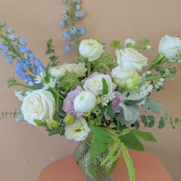 Mixed bouquet of white roses, pale blooms, and blue flowers in a glass vase