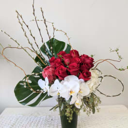 Red roses and white orchids in a tall vase with large leaves