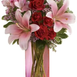 Pink lilies and red roses arranged in a tall pink vase
