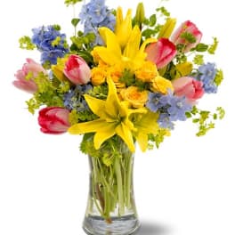 Colorful bouquet of tulips, lilies, and blue flowers in a glass vase
