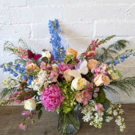 Mixed bouquet in a glass vase with pink, peach, white, and blue flowers