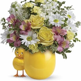 Yellow mug-shaped vase with mixed flowers and a chick figurine