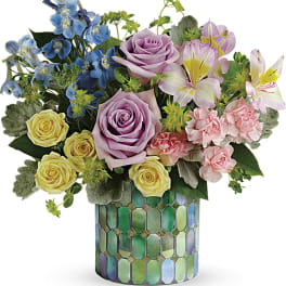 Mixed bouquet of roses, lilies, and blue flowers in a mosaic vase