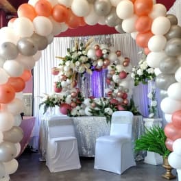 Balloon arch with white, peach, and silver balloons around floral displays