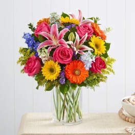 Mixed bouquet of pink roses, lilies, and bright daisies in a clear glass vase