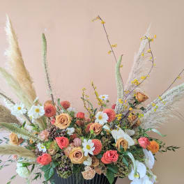 Large floral arrangement with peach roses, white orchids, and pampas grass in a black vase