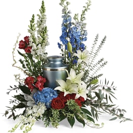 Sympathy arrangement with lilies, roses, and delphinium around a blue urn