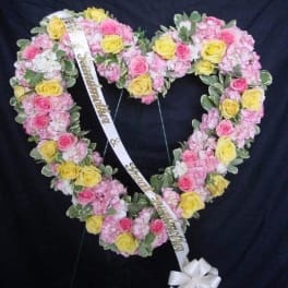 Heart-shaped floral wreath with pink and yellow roses and a white ribbon