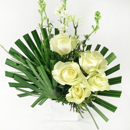 White roses arranged with tall white blooms in a white vase